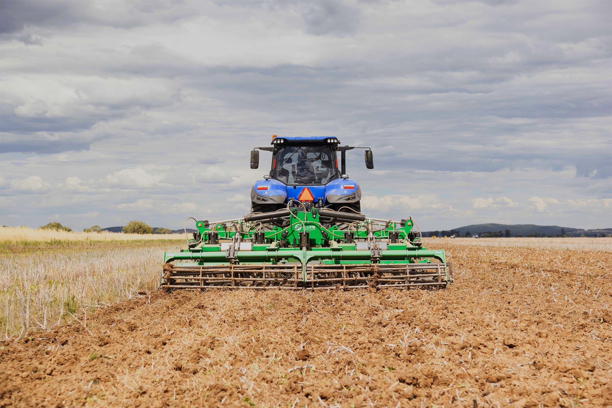 A K-Line Ag SpeedChisel machine being towed through a paddock by a blue tractor