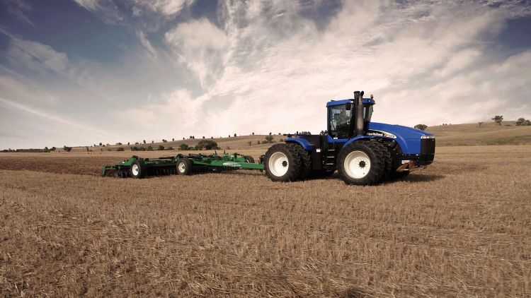 A K-Line Ag Speedtiller machine in a field of wheat stubble being pulled by a blue tractor